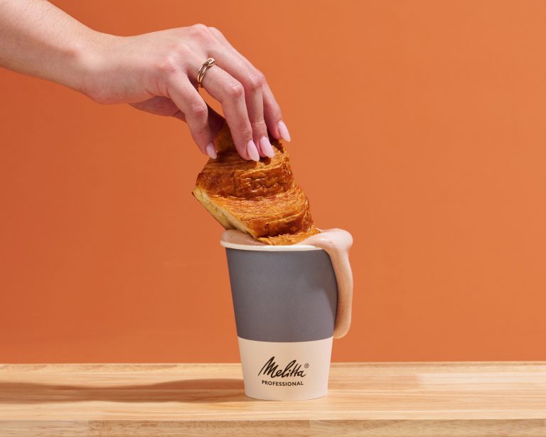 Styled product image of pastry being dipped into Melitta Coffee cup
